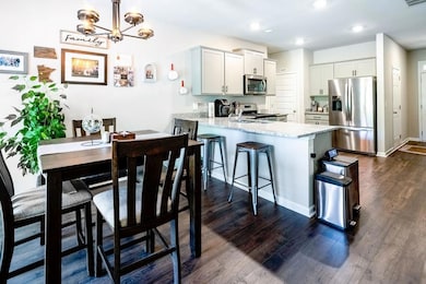 Kitchen featuring appliances with stainless steel finishes, a peninsula, dark wood finished floors, light stone counters, and a kitchen bar
