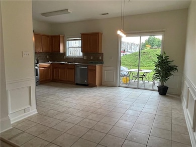 Kitchen with appliances with stainless steel finishes, a decorative wall, light tile patterned flooring, decorative backsplash, and a wainscoted wall