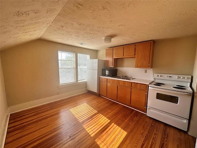 Kitchen featuring white appliances, dark wood-type flooring, light countertops, a sink, and lofted ceiling
