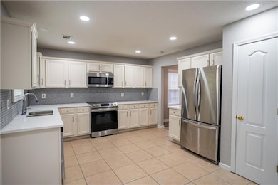 Kitchen with appliances with stainless steel finishes, light tile patterned flooring, decorative backsplash, light stone counters, and white cabinets