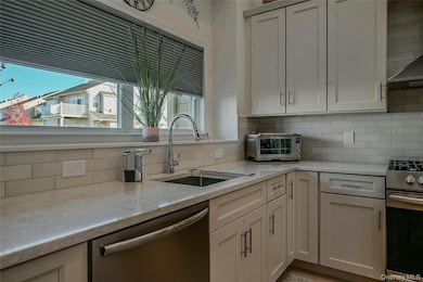 Kitchen with appliances with stainless steel finishes, decorative backsplash, ventilation hood, light stone countertops, and white cabinetry