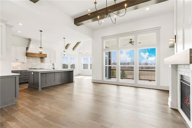 Kitchen featuring open floor plan, light countertops, custom range hood, an island with sink, and pendant lighting