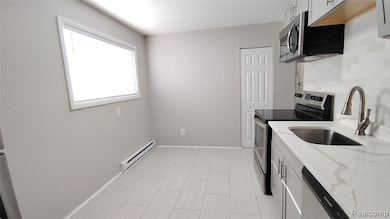 Kitchen with stainless steel appliances, light stone counters, a baseboard radiator, tasteful backsplash, and white cabinets