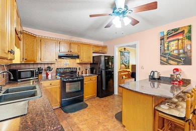 Kitchen with black appliances, under cabinet range hood, a sink, decorative backsplash, and a ceiling fan
