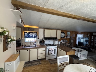 Kitchen featuring white gas range, dark wood-type flooring, white cabinets, a peninsula, and wooden walls