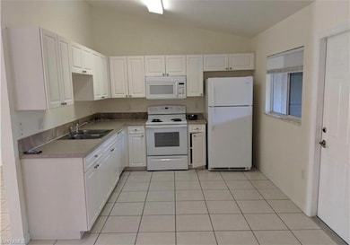 Kitchen featuring white appliances, white cabinets, lofted ceiling, light tile patterned flooring, and light countertops
