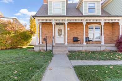 Property entrance featuring a lawn, brick siding, a porch, and roof with shingles