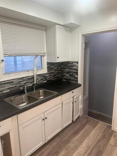 Kitchen with dark countertops, dark wood-type flooring, white cabinets, and backsplash