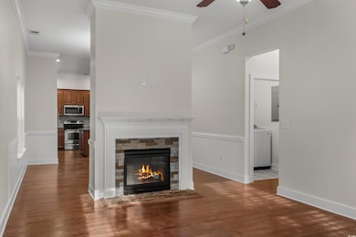 Unfurnished living room featuring ornamental molding, dark wood finished floors, a fireplace, a ceiling fan, and washer / dryer