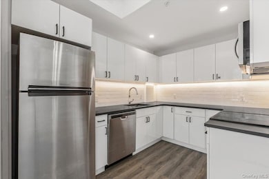 Kitchen with stainless steel appliances, white cabinetry, dark wood-style flooring, tasteful backsplash, and recessed lighting