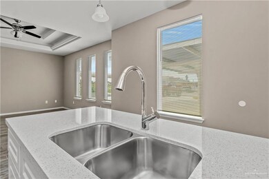 Kitchen with light stone countertops, sink, a tray ceiling, and ceiling fan