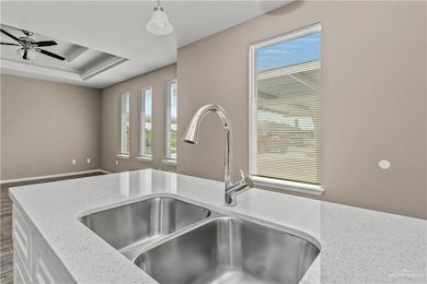 Kitchen with light stone countertops, sink, a tray ceiling, and ceiling fan