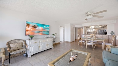 Living area with a textured ceiling, light tile patterned floors, a ceiling fan, and a chandelier