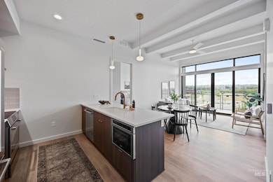 Kitchen featuring modern cabinets, a peninsula, light wood finished floors, hanging light fixtures, and beamed ceiling