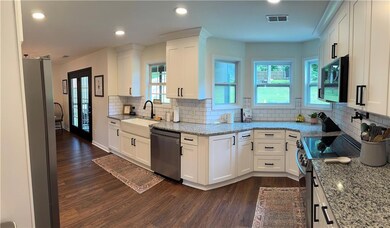 Kitchen with stainless steel appliances, a farm sink, dark wood-type flooring, white cabinetry, and decorative backsplash