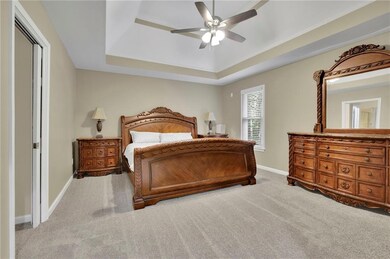 Bedroom with light colored carpet, a tray ceiling, and a ceiling fan