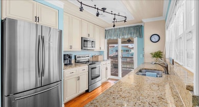 Kitchen featuring appliances with stainless steel finishes, ornamental molding, track lighting, light stone countertops, and light wood finished floors