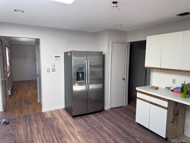 Kitchen featuring stainless steel fridge with ice dispenser, white cabinetry, light countertops, dark wood-type flooring, and recessed lighting
