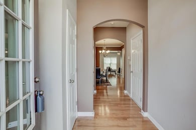Corridor featuring arched walkways, light wood-style flooring, a chandelier, and ornamental molding