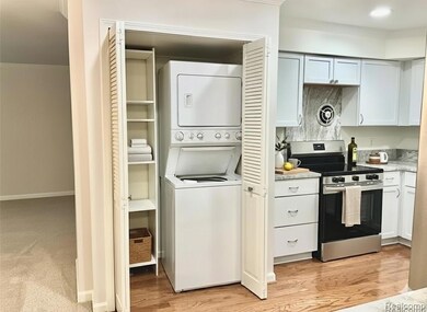 Kitchen featuring stainless steel range with electric stovetop, ornamental molding, stacked washer / dryer, light wood-type flooring, and white cabinetry