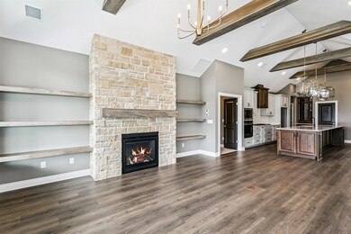 Kitchen featuring a chandelier, beamed ceiling, pendant lighting, a fireplace, and an island with sink