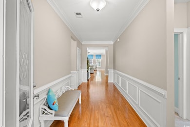 Hallway featuring crown molding, light wood-style floors, a wainscoted wall, and a decorative wall