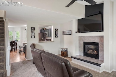 Carpeted living room with stairs, ceiling fan, a tile fireplace, and baseboards