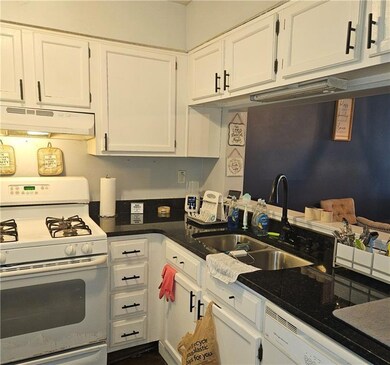 Kitchen featuring white appliances, under cabinet range hood, a sink, and white cabinets