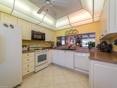 Kitchen with white appliances, dark countertops, a sink, a ceiling fan, and light tile patterned floors