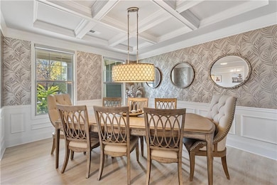 Dining room featuring wallpapered walls, a decorative wall, a wainscoted wall, and light wood-style floors