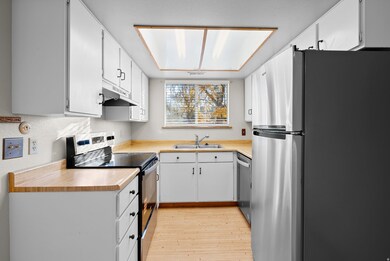 Kitchen featuring appliances with stainless steel finishes, light countertops, light wood-style flooring, and white cabinets