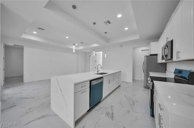 Kitchen featuring a tray ceiling, electric stove, white cabinets, light stone counters, and recessed lighting