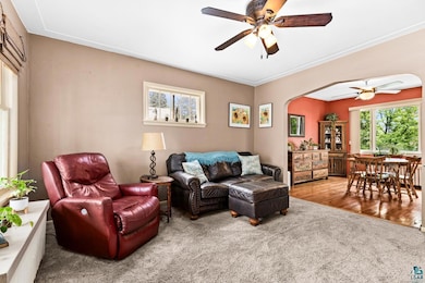 Living area with a ceiling fan, arched walkways, carpet floors, and crown molding