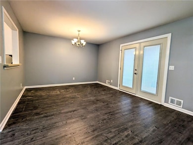 Unfurnished room featuring french doors, dark wood-style flooring, and a chandelier
