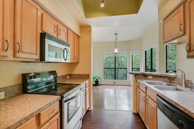 Kitchen featuring appliances with stainless steel finishes, pendant lighting, dark wood finished floors, light countertops, and a tray ceiling
