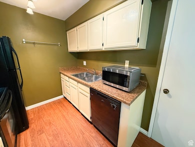 Kitchen with black appliances, light wood-style floors, white cabinets, and light countertops