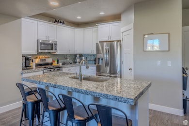 Kitchen featuring decorative backsplash, stainless steel appliances, white cabinetry, a kitchen breakfast bar, and a center island with sink
