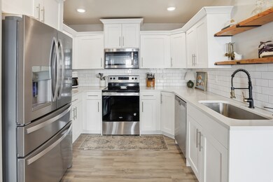 Kitchen featuring stainless steel appliances, white cabinetry, open shelves, light stone counters, and recessed lighting