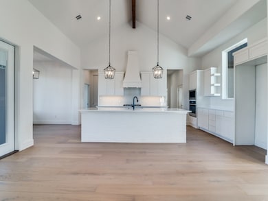 Kitchen featuring white cabinetry, light wood-style floors, an island with sink, beam ceiling, and custom range hood