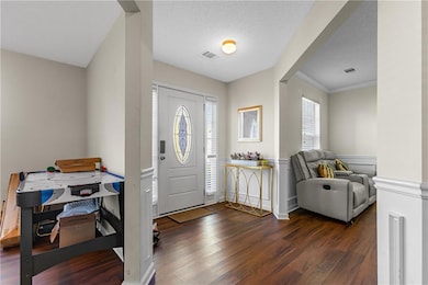 Entrance foyer featuring dark wood-style floors, a textured ceiling, ornamental molding, and a wainscoted wall