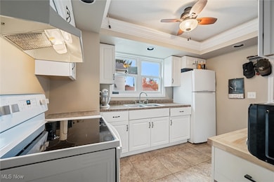 Kitchen with white appliances, under cabinet range hood, white cabinetry, a tray ceiling, and ornamental molding