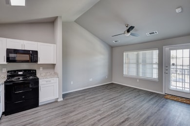 Kitchen with black appliances, vaulted ceiling, light wood finished floors, white cabinetry, and a ceiling fan