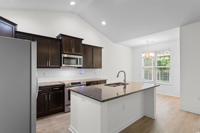 Kitchen with stainless steel appliances, vaulted ceiling, dark stone countertops, light wood-type flooring, and backsplash