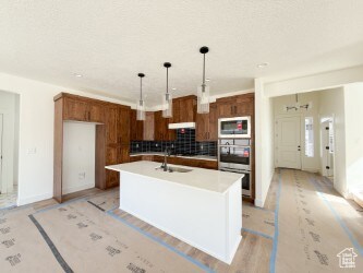Kitchen featuring brown cabinetry, backsplash, decorative light fixtures, light countertops, and an island with sink
