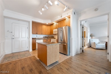 Kitchen with sink, ornamental molding, a center island, white appliances, and light hardwood / wood-style flooring