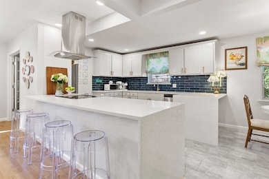 Kitchen featuring a peninsula, white cabinets, tasteful backsplash, a kitchen breakfast bar, and island exhaust hood