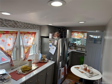 Kitchen with gray cabinets, appliances with stainless steel finishes, light stone countertops, dark wood-type flooring, and recessed lighting