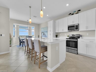 Kitchen featuring stainless steel appliances, a center island with sink, light countertops, white cabinetry, and pendant lighting