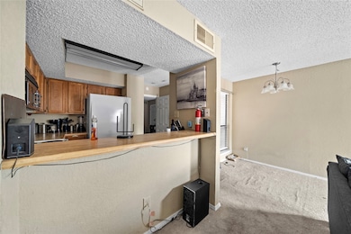 Kitchen with light colored carpet, light countertops, white refrigerator, brown cabinetry, and a textured ceiling