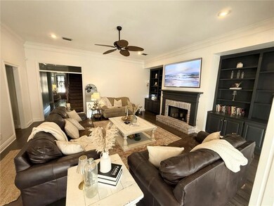 Living room featuring wood finished floors, built in shelves, a fireplace, a ceiling fan, and ornamental molding
